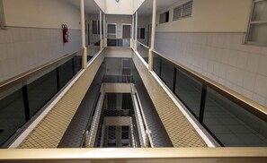 Ein Korridor mit zentralem Gehweg, Glasgeländern, gefliesten Wänden und einem Feuerlöscher links.