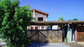 A residential building with a tiled roof, a wooden gate, and a tree in the foreground. - Casa com ótima localização e churrasqueira (Ilhabela)