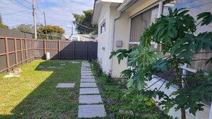 A residential backyard with a stone pathway, a wooden fence, and a fig tree. - Modern Ceramic Retreat - Newly Remodeled 2BR/2BA (North Miami Beach)