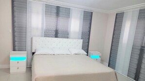 A bedroom with a large bed, two bedside tables, and a window with striped curtains. - Modern Ceramic Retreat - Newly Remodeled 2BR/2BA (North Miami Beach)