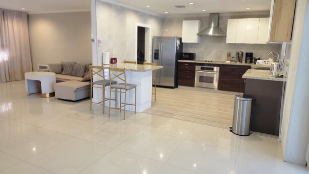 A modern kitchen with a central island, built-in appliances, and a dining area with a sofa and chairs. - Modern Ceramic Retreat - Newly Remodeled 2BR/2BA (North Miami Beach)