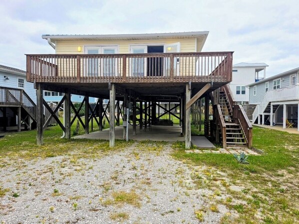 Ein zweistöckiges Haus mit einer Holzterrasse und einer Treppe, die zum Obergeschoss führt.