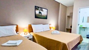 A hotel room with two beds, each with a white pillow and a folded towel. There is a nightstand with a lamp, a painting of a horse on the wall, and a bathroom visible through an open door.