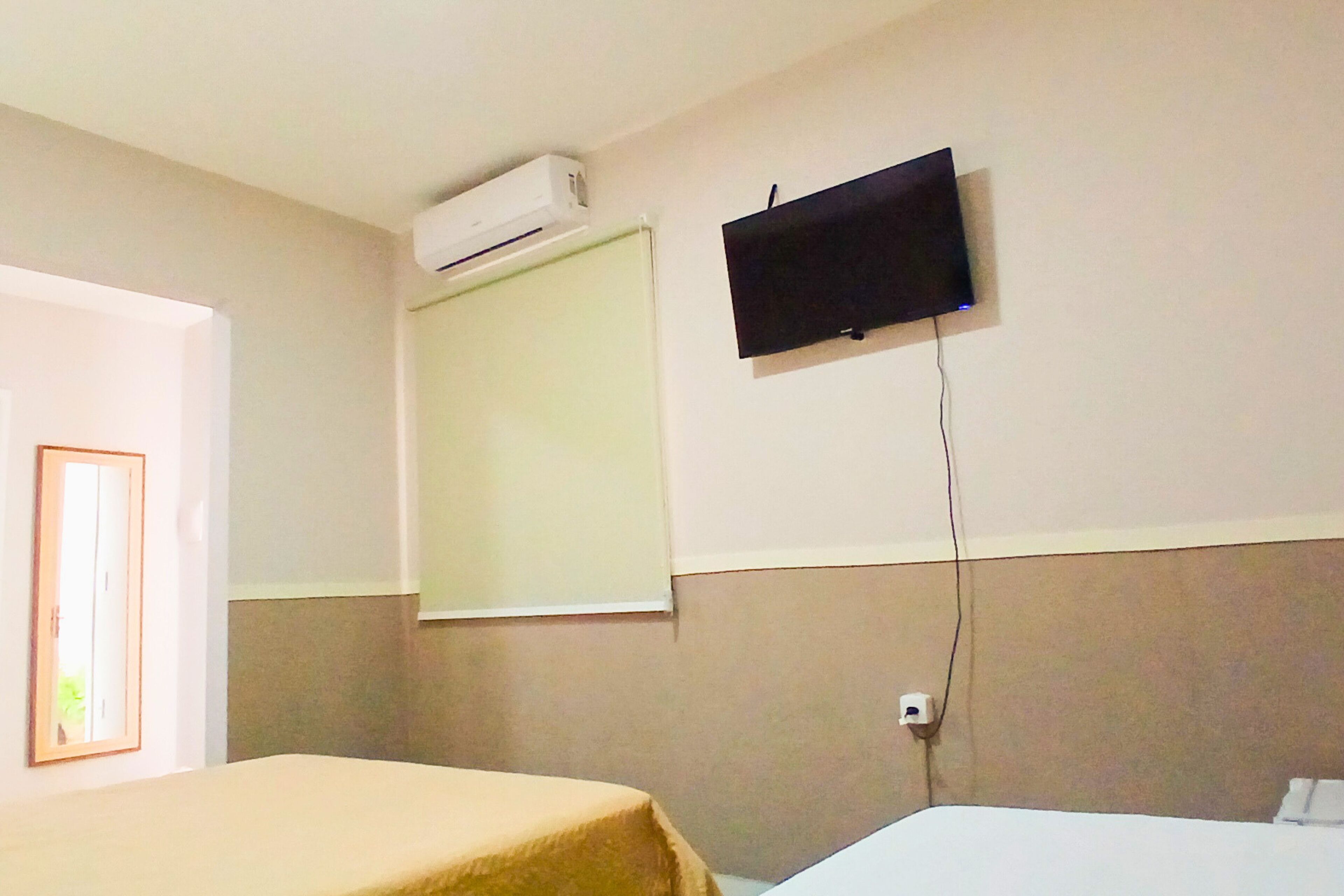 A hotel room with a bed, a television mounted on the wall, and an air conditioning unit.