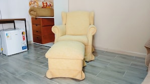 A room with a beige recliner, a small table, a white refrigerator, and a wooden cabinet.