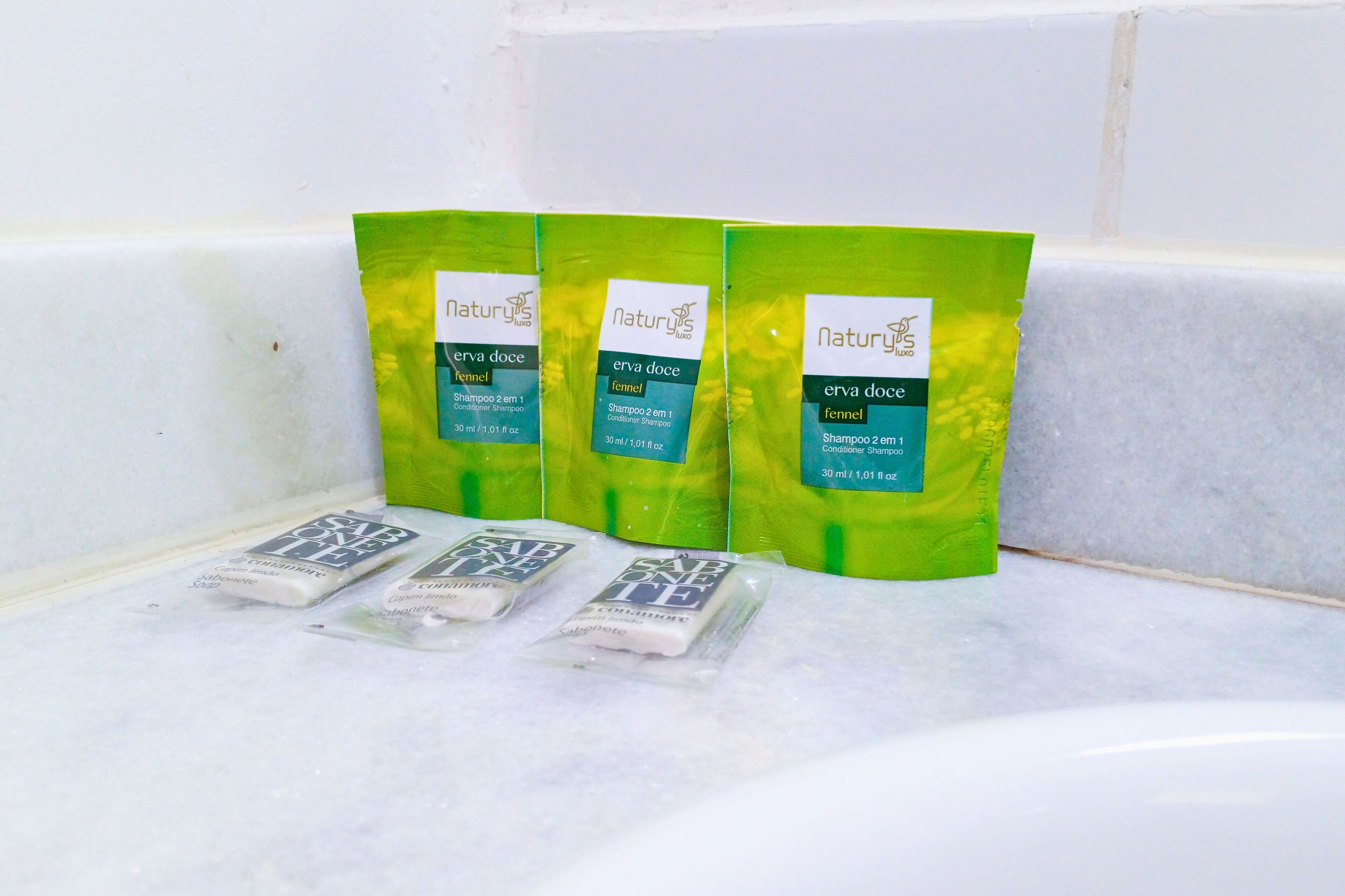 Three green bags of shampoo and two smaller packets on a white surface.