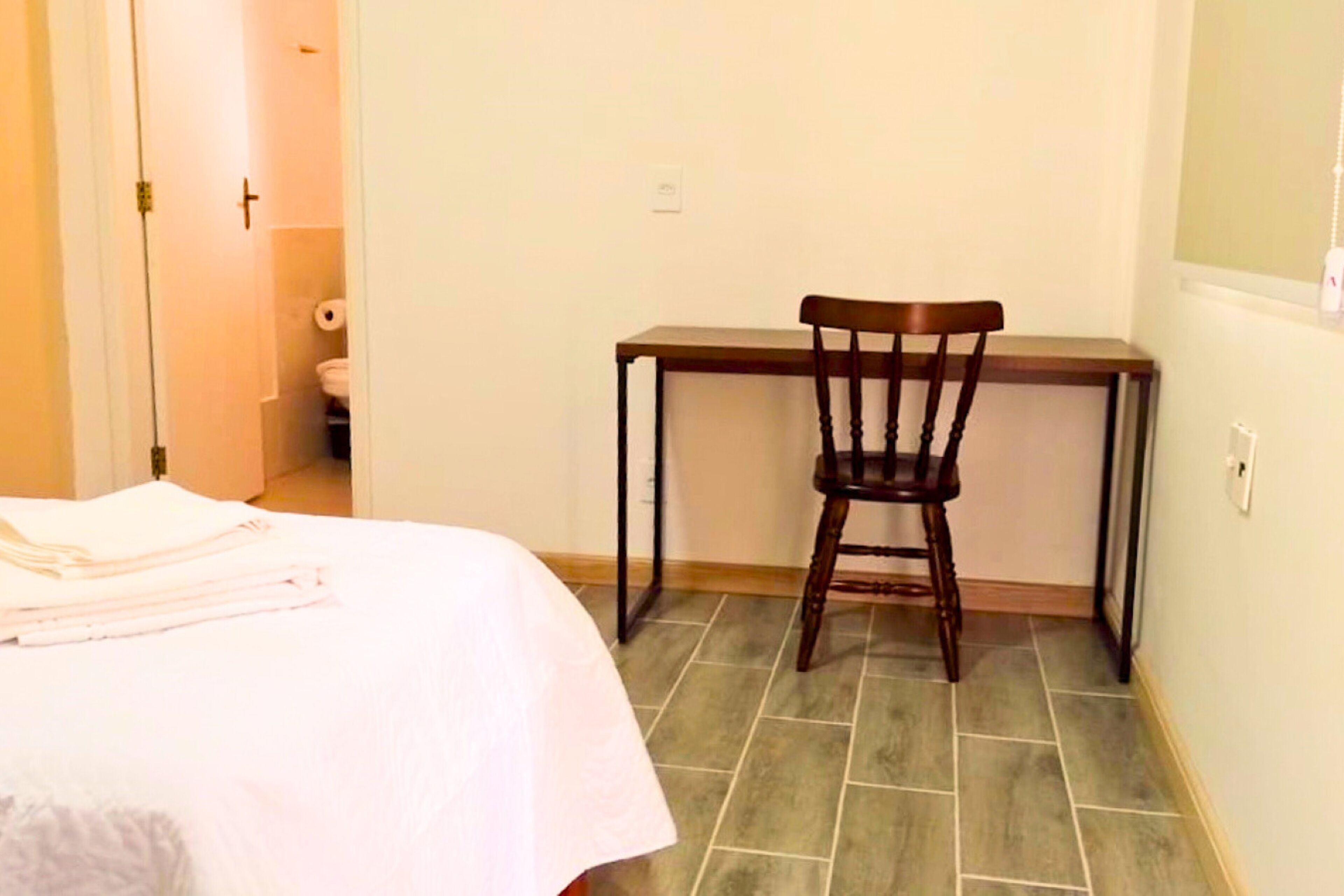 A bedroom with a bed, a desk, and a chair. There is a door leading to a bathroom.