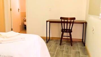 A bedroom with a bed, a desk, and a chair. There is a door leading to a bathroom.