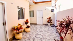 A corridor with tiled flooring, potted plants, a white door, and a window.