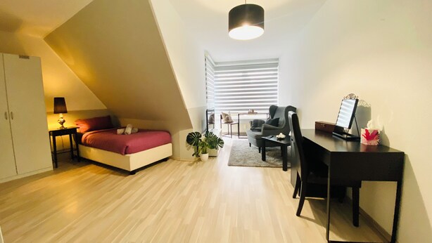Un appartement moderne et compact doté d’un plafond en pente, d’un lit, d’un bureau et d’une chaise.