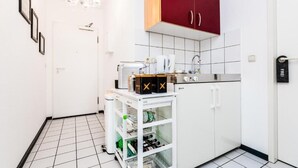 Une cuisine compacte avec des meubles blancs, un meuble supérieur rouge, un plan de travail blanc et un petit réfrigérateur blanc.