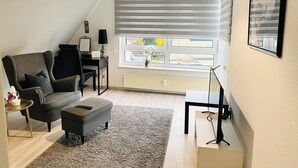 Un salon moderne avec un canapé, un pouf et une petite table sur laquelle se trouve une lampe.