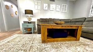 A living room with a grey sofa, a wooden coffee table, a side table, a lamp, and wall art. - Midcity Sunrise (Lake Charles)