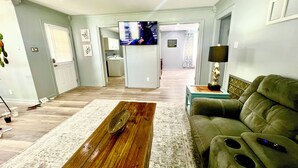A living room with a wooden coffee table, a green sofa, and a TV in the background. - Midcity Sunrise (Lake Charles)