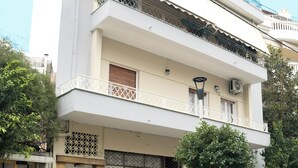 Ein zweigeschossiges Gebäude mit weißer Fassade, einem Balkon mit Metallgeländer und einem Baum davor.