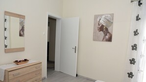 Ein Schlafzimmer mit einem hölzernen Schminktisch, einem Bett mit gemustertem Überwurf, einem Bild an der Wand und einer Tür zu einem anderen Raum.