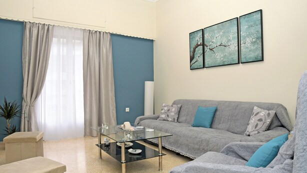 Ein modernes Wohnzimmer mit einem Glastisch, grauem Sofa und blauen Wänden.