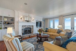 A living room with a fireplace, a sofa, a striped armchair, and a view of the sea through large windows. - Dog Friendly-Luxury home on Lake Michigan (Sturgeon Bay)