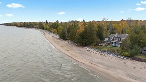 Ein Strandhaus mit sandigem Ufer, Blick auf das Wasser und bewaldeter Umgebung.