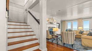 Eine Treppe führt in ein Wohnzimmer mit Kamin, einer Couch und Meerblick.