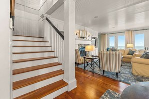 Una escalera conduce a una sala de estar con chimenea, un sofá y vistas al mar.