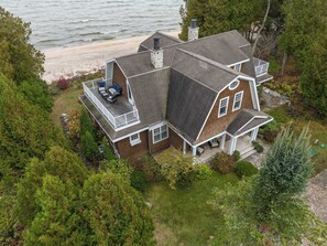 A two-story house with a balcony, a stone chimney, and a view of the beach. - Dog Friendly-Luxury home on Lake Michigan (Sturgeon Bay)