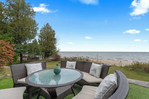 Ein runder Glastisch mit Korbstühlen und Kissen, mit Blick auf einen Strand.