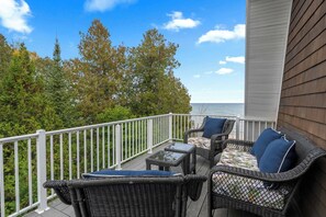 A balcony with wicker furniture, a glass table, and a view of the ocean. - Dog Friendly-Luxury home on Lake Michigan (Sturgeon Bay)