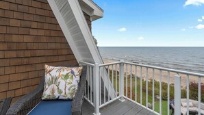 Ein Balkon mit Blick auf das Meer, ein Korbstuhl und ein Kissen mit tropischem Muster.