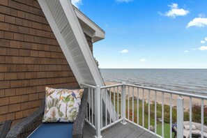 A balcony with a view of the ocean, a wicker chair, and a cushion with a tropical print. - Dog Friendly-Luxury home on Lake Michigan (Sturgeon Bay)