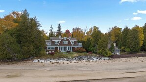 Ein Strandhaus mit großer Veranda, umgeben von Bäumen und einem Sandstrand.