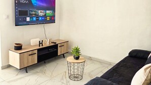 Une chambre à coucher moderne avec un téléviseur à écran plat fixé au mur, une table de chevet en bois, une petite plante en pot, un canapé noir et un sol carrelé en marbre.