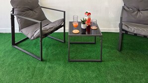 Une pièce comprenant deux fauteuils gris, une petite table avec une boisson et une boîte de carton, et un tableau représentant une scène de plage accroché au mur.