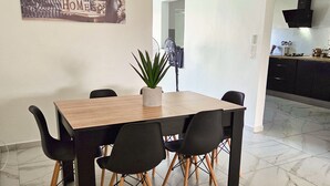 Un coin repas avec une table en bois, des chaises noires, une plante en pot et une cuisine en arrière-plan.