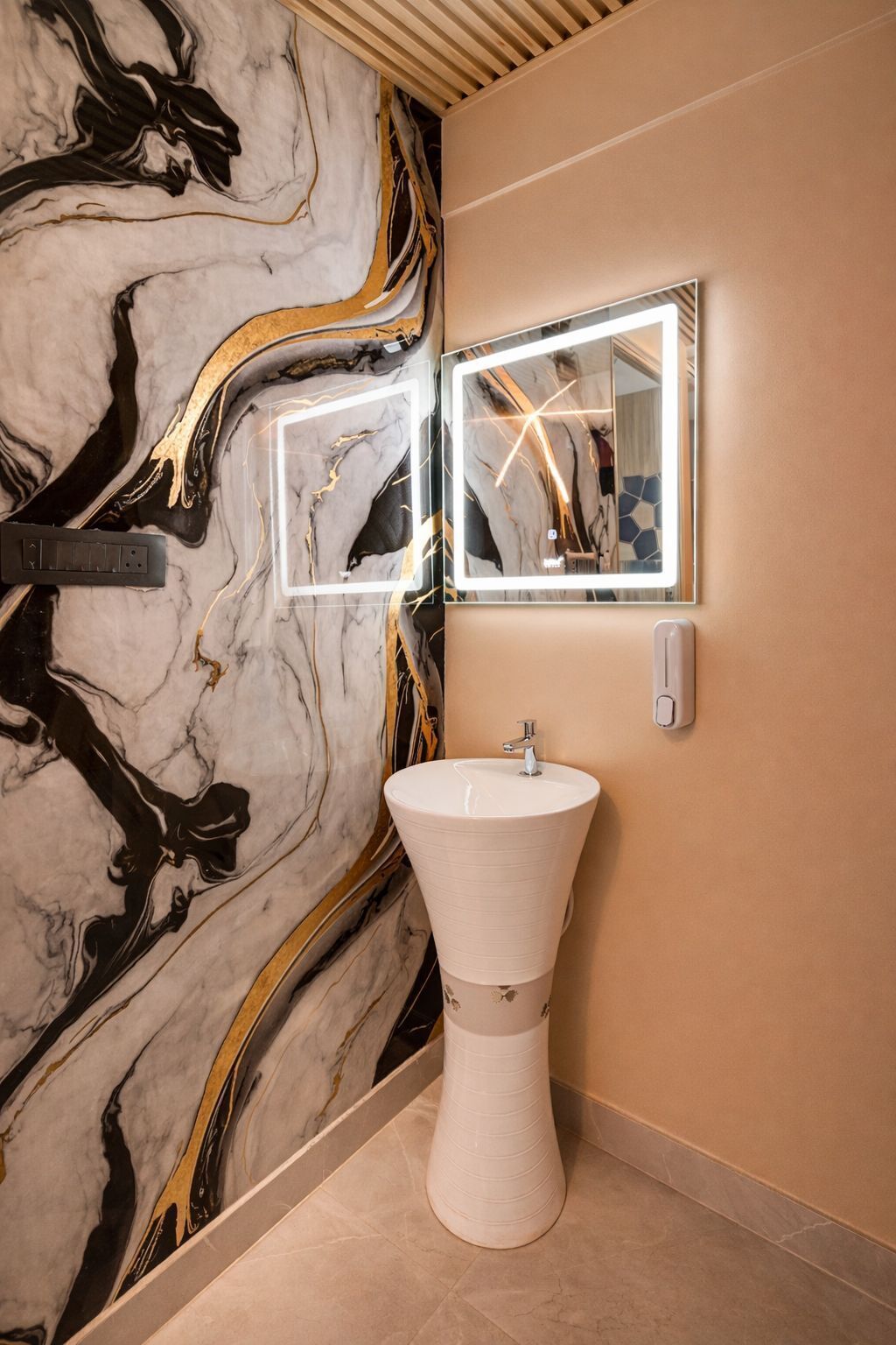 Une salle de bain avec un mur en marbre, un lavabo blanc et un miroir doté d’une bande lumineuse.
