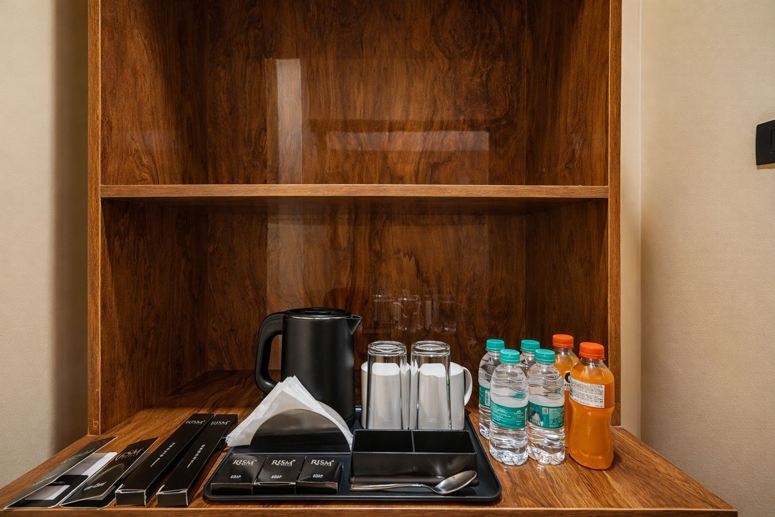 A wooden cabinet with a coffee maker, water bottles, and a tray with utensils.