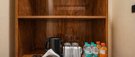 A wooden cabinet with a coffee maker, water bottles, and a tray with utensils.