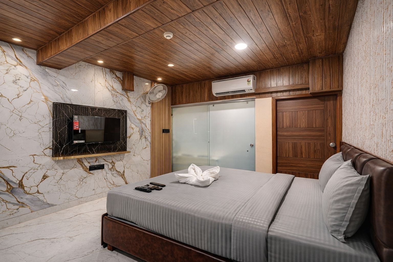 Quarto moderno com parede de mármore, televisão na parede, guarda-roupa e cama com toalha.