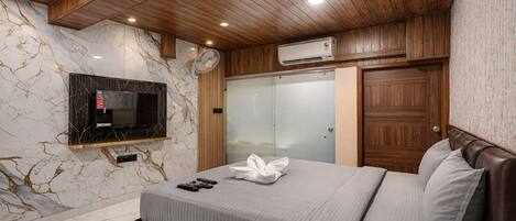 Quarto moderno com parede de mármore, televisão na parede, guarda-roupa e cama com toalha.