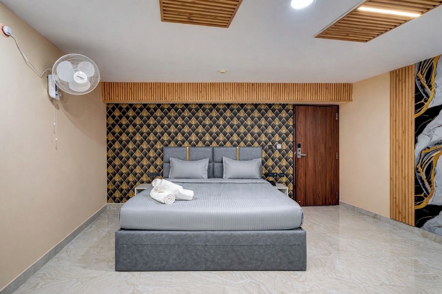 A modern bedroom with a large bed, a wall-mounted fan, and a patterned wallpaper.