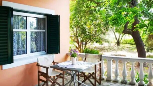 Un patio con mesa y sillas, una ventana con contraventanas y vistas a follaje.