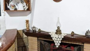 Una habitación acogedora con una repisa de madera, una chimenea con un tapete decorativo y una estantería con juegos de té y una planta en maceta.