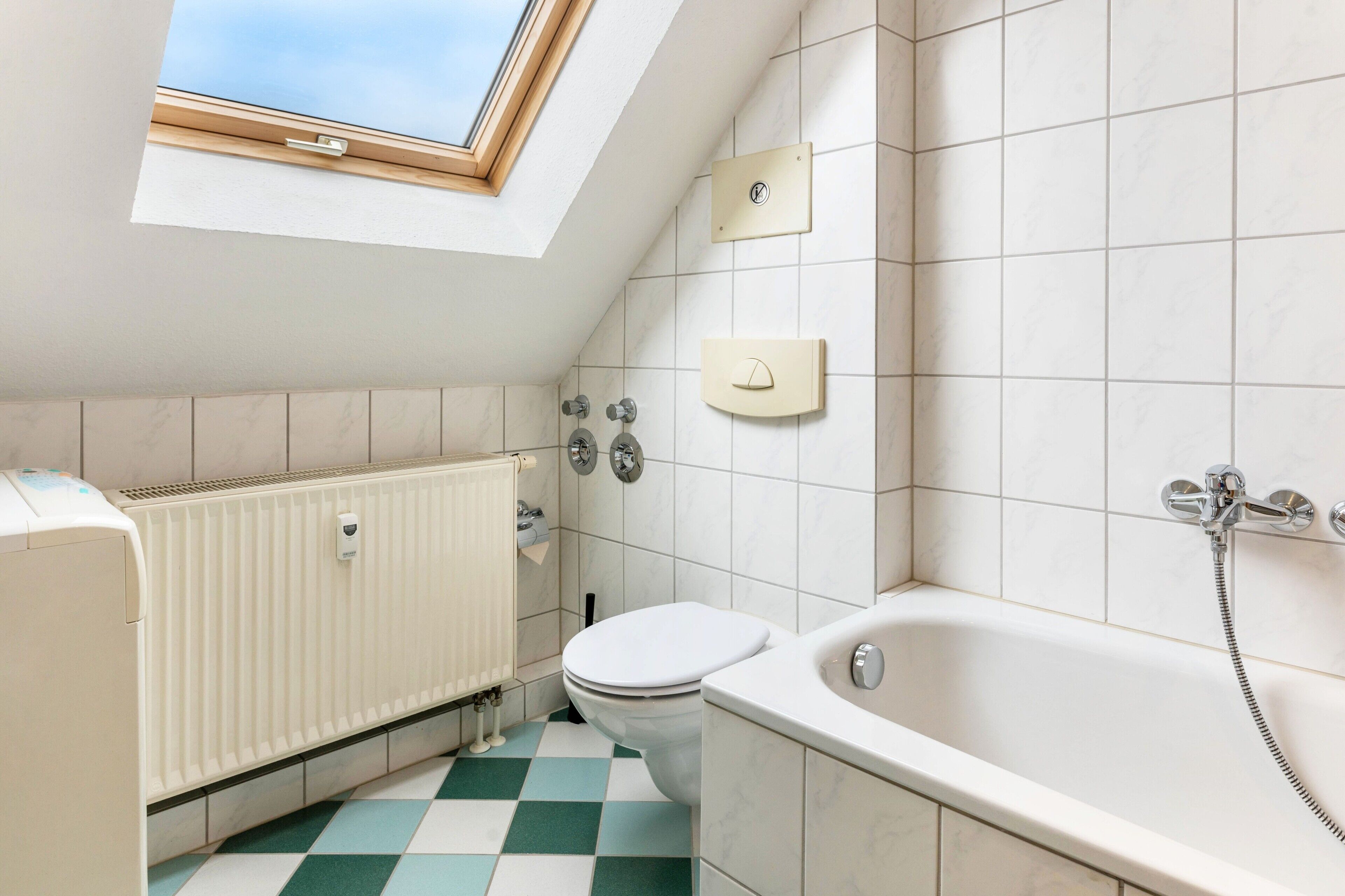 A modern bathroom with a skylight, a white radiator, a toilet, and a bathtub.