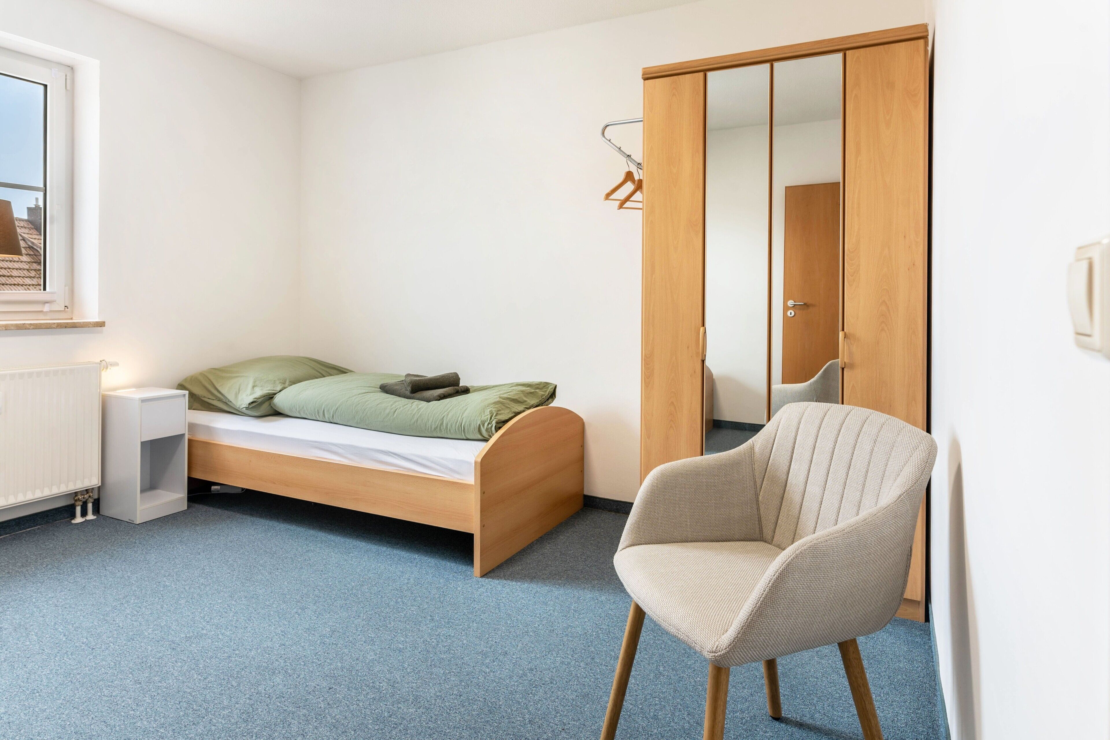 Een slaapkamer met een enkel bed, een stoel, een kledingkast en een radiator.