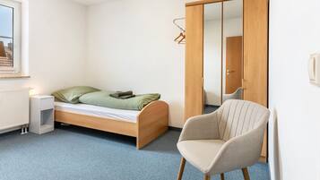 Een slaapkamer met een enkel bed, een stoel, een kledingkast en een radiator.