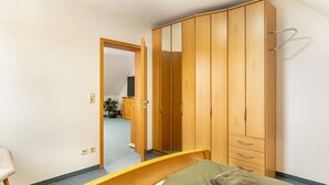 Une chambre à coucher comprenant un lit, une armoire en bois, une chaise et une porte donnant sur une autre pièce.