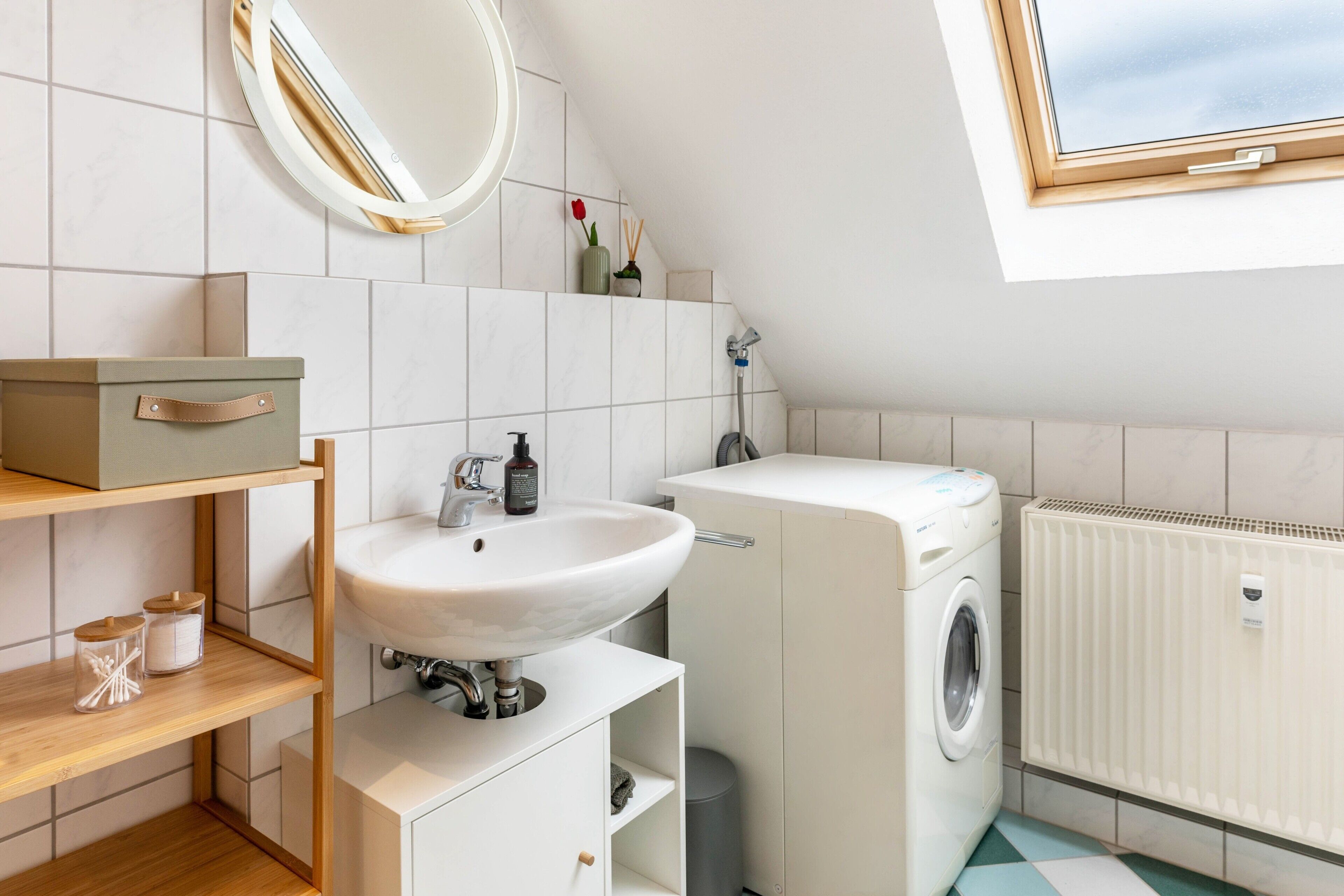 A modern bathroom with a sink, mirror, shelf, and a washing machine.