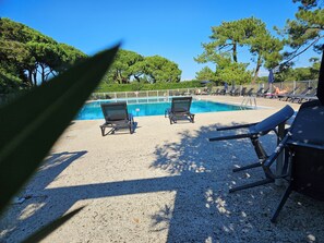 A pool area with two lounge chairs and a table, surrounded by trees and a fence. - Air-conditioned 3-star studio in Anglet Chiberta, ocean views, golf, 200 meters from the beach, pool. (Anglet)