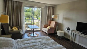Ein Hotelzimmer mit einem großen Bett, einer Couch, einem Sessel, einem kleinen Tisch, einem Fernseher, einem Ventilator und Blick ins Freie.