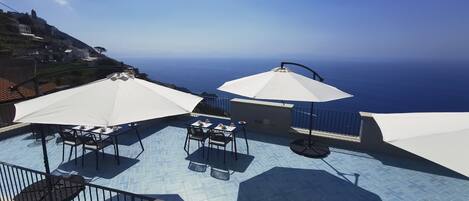 Une terrasse sur le toit, dotée de sièges extérieurs et de parasols, offrant une vue sur la côte.